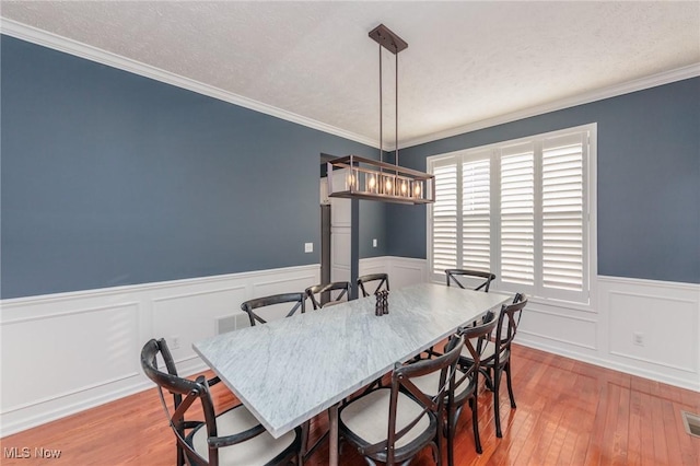 dining space with light wood finished floors, crown molding, a textured ceiling, and wainscoting