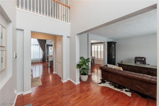 living room with a high ceiling, a textured ceiling, baseboards, and wood finished floors