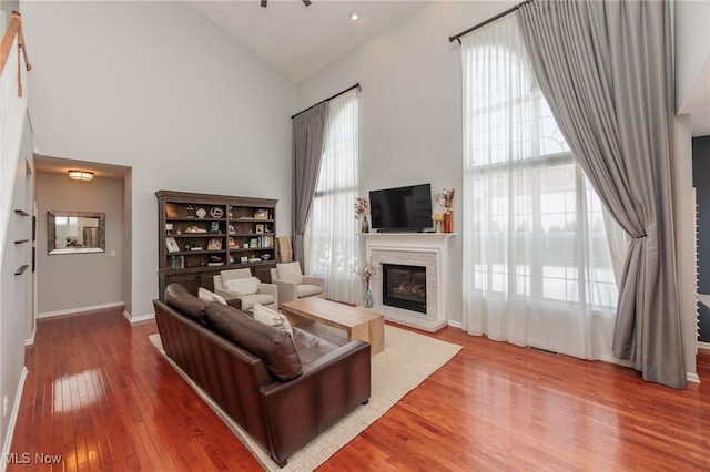 living area with high vaulted ceiling, a wealth of natural light, a brick fireplace, and wood finished floors