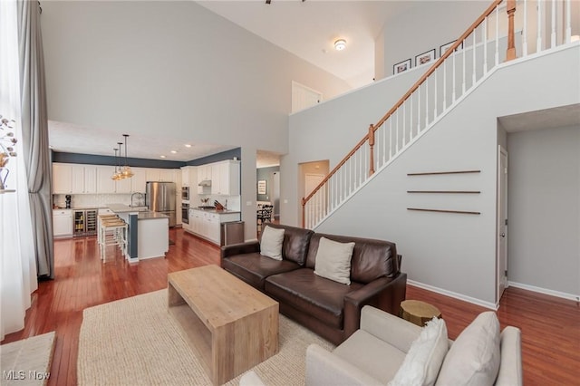 living room featuring beverage cooler, a high ceiling, baseboards, stairway, and light wood-type flooring