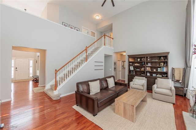 living area with a towering ceiling, stairs, baseboards, and wood finished floors