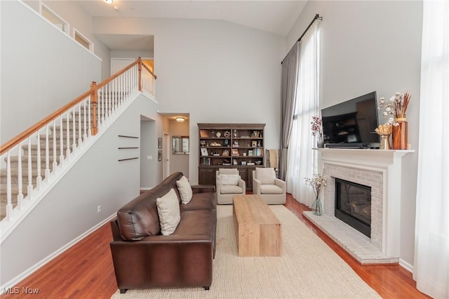 living area featuring stairway, a brick fireplace, high vaulted ceiling, and light wood-style flooring