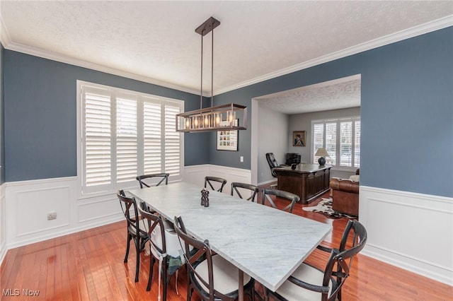 dining room featuring a wainscoted wall, crown molding, a textured ceiling, and light wood-style floors