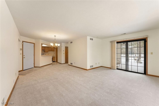 spare room with baseboards, an inviting chandelier, visible vents, and light colored carpet