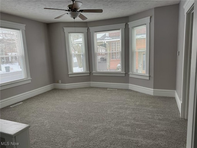 carpeted empty room featuring a textured ceiling, a ceiling fan, visible vents, and baseboards