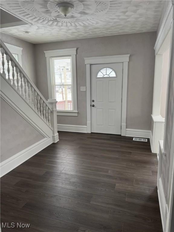 foyer with stairs, dark wood finished floors, visible vents, and baseboards