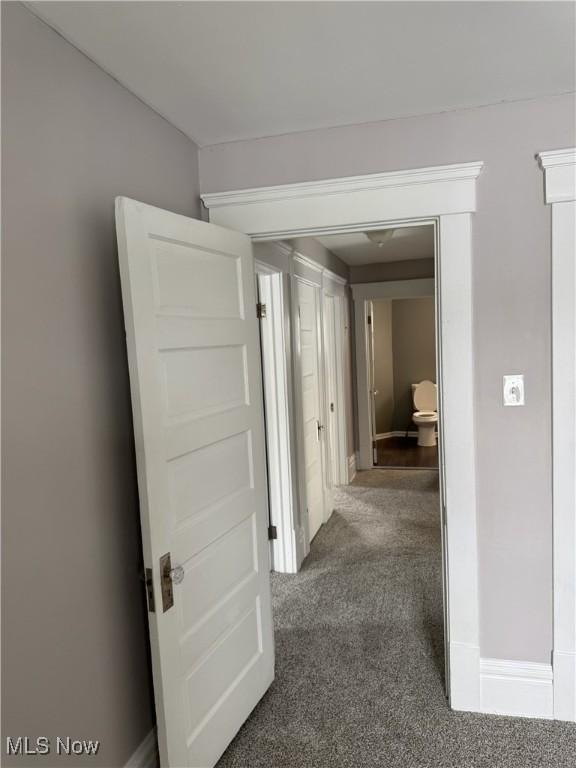 hallway featuring dark carpet and baseboards