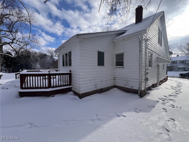 view of snow covered exterior featuring a chimney and a wooden deck