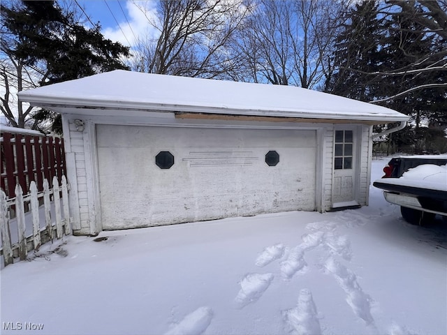 snow covered garage with a detached garage and fence