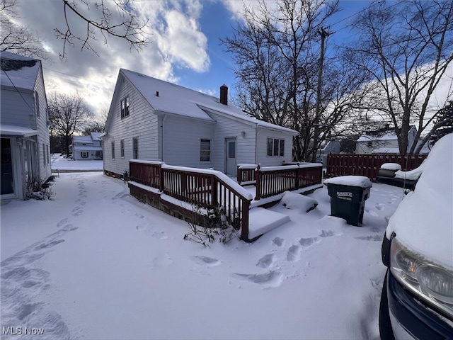 snow covered property with a garage, a chimney, fence, and a deck