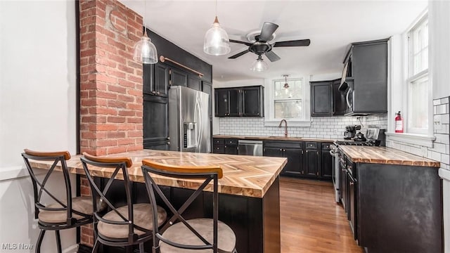 kitchen featuring butcher block counters, appliances with stainless steel finishes, a sink, a peninsula, and a kitchen bar