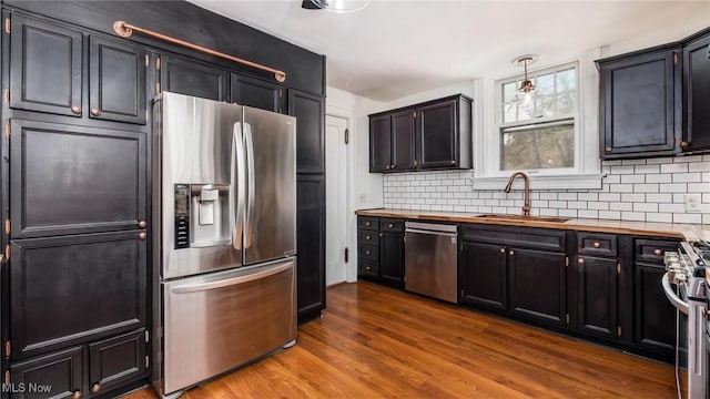 kitchen with stainless steel appliances, wood finished floors, a sink, hanging light fixtures, and wooden counters