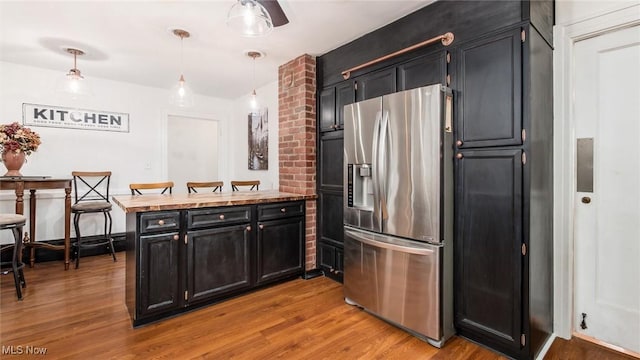 kitchen with hanging light fixtures, light wood-type flooring, stainless steel fridge, and dark cabinets