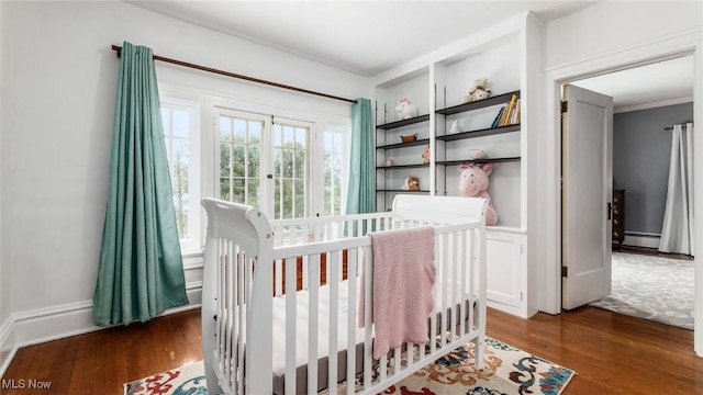 bedroom with a crib, a baseboard radiator, and dark wood-type flooring