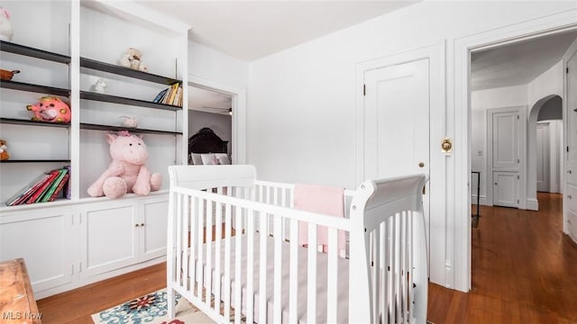 bedroom with a nursery area, arched walkways, and wood finished floors