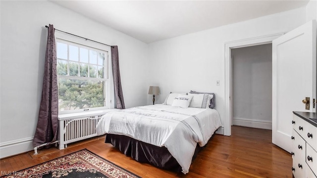 bedroom featuring radiator heating unit, baseboards, and dark wood-type flooring