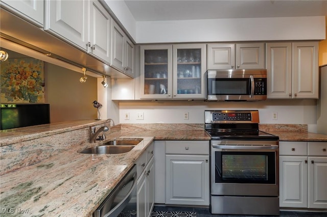 kitchen with light stone counters, glass insert cabinets, stainless steel appliances, and a sink