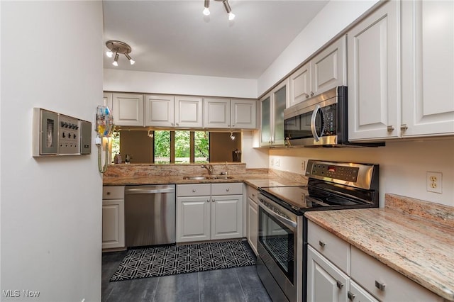 kitchen featuring light stone counters, glass insert cabinets, stainless steel appliances, and a sink