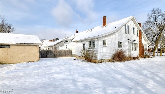 snow covered rear of property with a chimney and fence