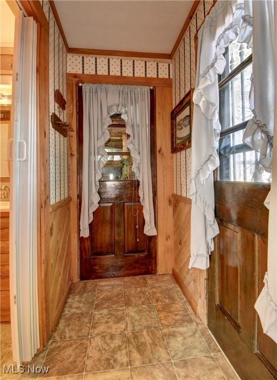 doorway with crown molding and wallpapered walls