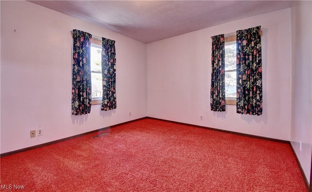 carpeted empty room with a textured ceiling, visible vents, and baseboards