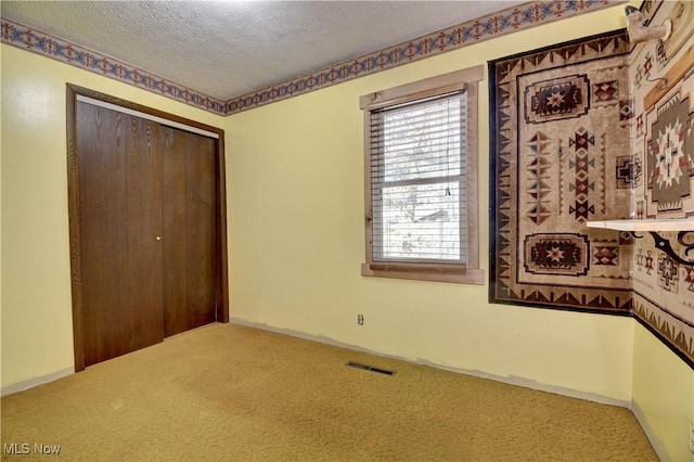 unfurnished bedroom featuring a textured ceiling, carpet floors, a closet, and visible vents