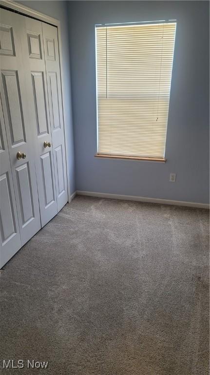 unfurnished bedroom featuring carpet, a closet, multiple windows, and baseboards