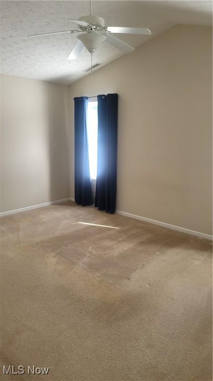 carpeted spare room with lofted ceiling, visible vents, ceiling fan, and baseboards