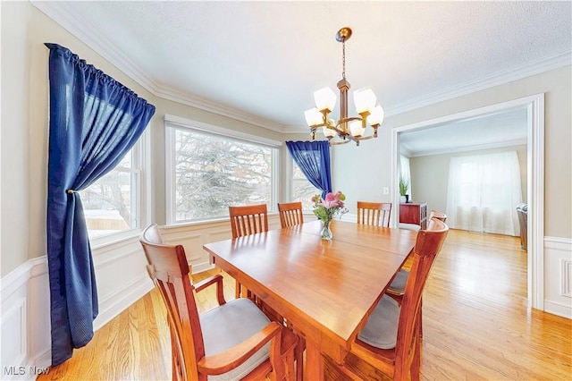 dining room featuring ornamental molding, a chandelier, a wainscoted wall, and light wood-style floors