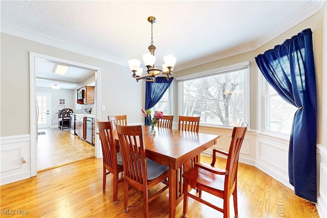 dining area featuring a wainscoted wall, crown molding, a notable chandelier, a decorative wall, and light wood-type flooring