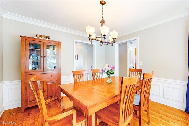 dining space with ornamental molding, light wood-type flooring, wainscoting, and a notable chandelier