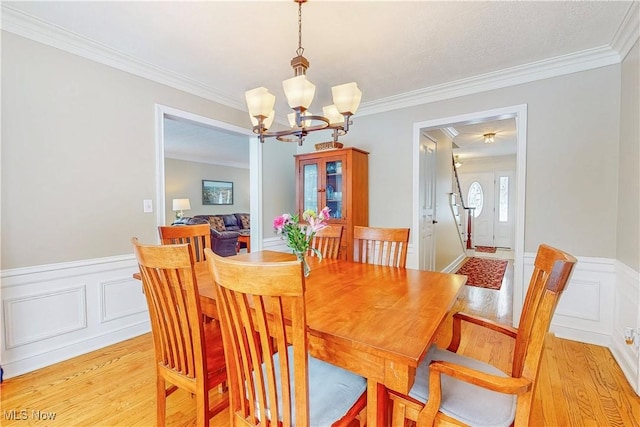 dining room featuring light wood-style floors, a wainscoted wall, ornamental molding, and an inviting chandelier