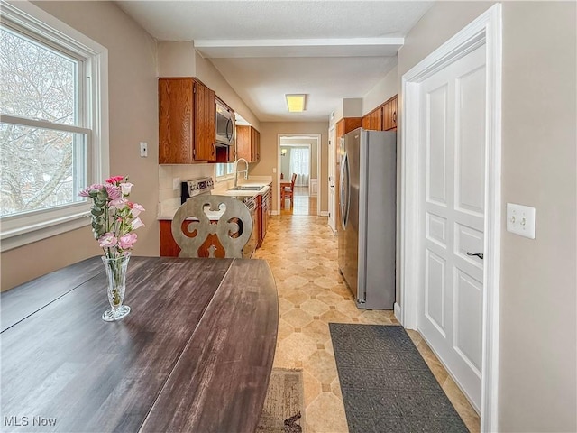 kitchen with light countertops, appliances with stainless steel finishes, a sink, and brown cabinets