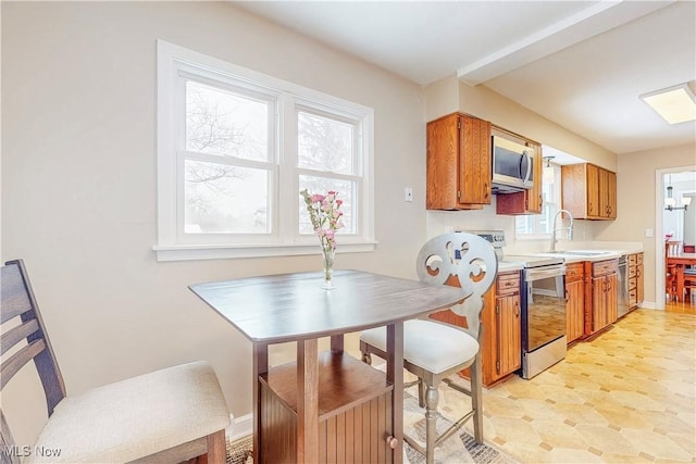 kitchen with a sink, baseboards, light countertops, appliances with stainless steel finishes, and brown cabinetry