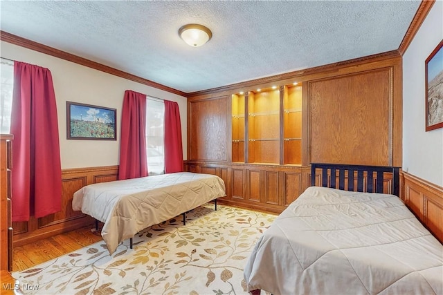 bedroom featuring light wood-type flooring, a wainscoted wall, ornamental molding, and a textured ceiling