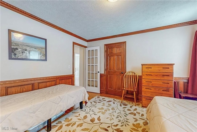 bedroom with a wainscoted wall, ornamental molding, and a textured ceiling