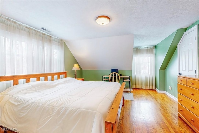 bedroom featuring visible vents, light wood-style floors, vaulted ceiling, a textured ceiling, and baseboards