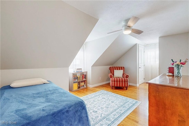 bedroom with light wood-style floors, vaulted ceiling, a textured ceiling, ceiling fan, and baseboards