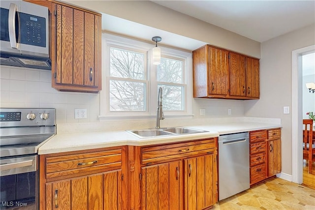 kitchen with appliances with stainless steel finishes, decorative light fixtures, a sink, light countertops, and backsplash