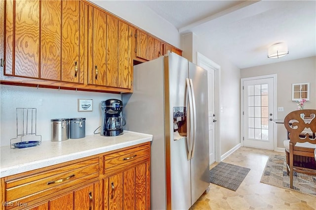 kitchen with baseboards, light countertops, light floors, brown cabinetry, and stainless steel fridge