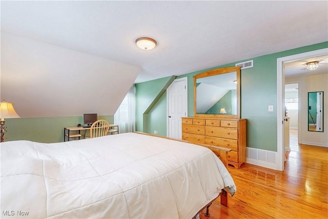 bedroom with light wood-type flooring, baseboards, visible vents, and lofted ceiling