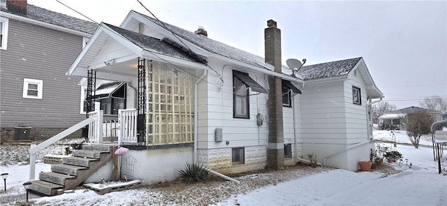 view of snowy exterior with central air condition unit and a chimney