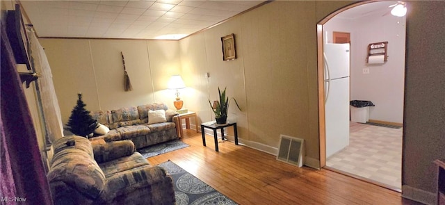 living area featuring light wood-style floors, visible vents, arched walkways, and crown molding