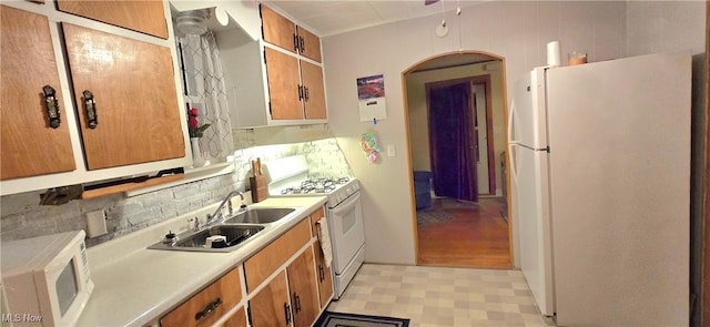 kitchen featuring arched walkways, light floors, light countertops, a sink, and white appliances