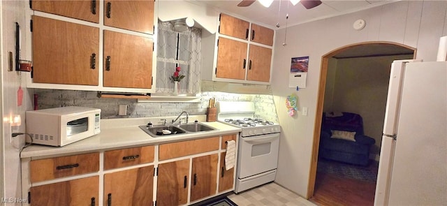 kitchen featuring arched walkways, white appliances, a sink, light countertops, and backsplash