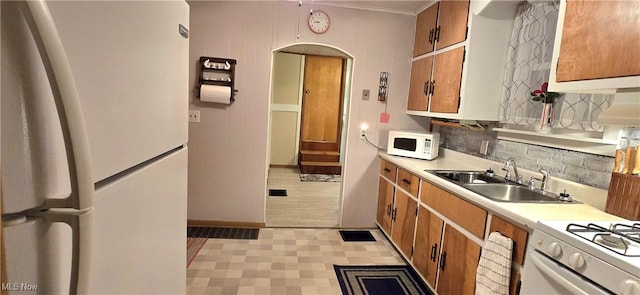 kitchen with arched walkways, brown cabinets, light countertops, a sink, and white appliances