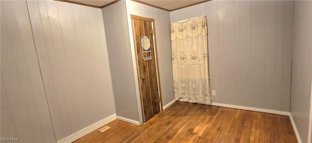 hall featuring ornamental molding, dark wood-style flooring, wood walls, and baseboards