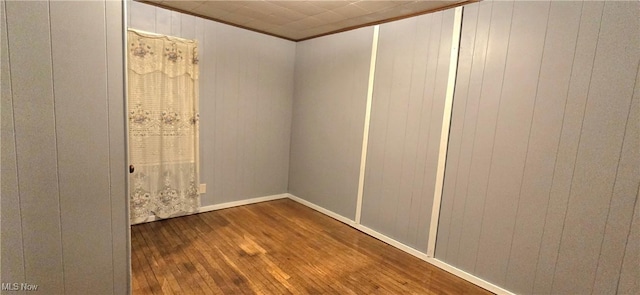 unfurnished room with wooden walls, ornamental molding, and wood finished floors