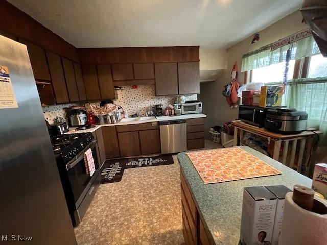 kitchen with light countertops, appliances with stainless steel finishes, a sink, and tasteful backsplash