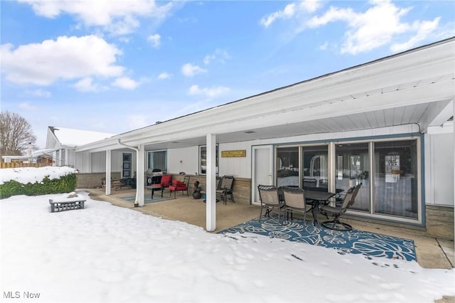 snow covered rear of property featuring a patio